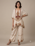 Model wearing an elegant cream-colored printed tunic and matching trousers set against a muted beige background.