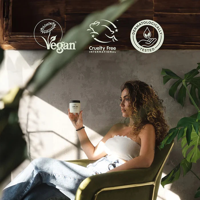 Woman holding a curl jar in a sunlit room with 'Vegan', 'Cruelty Free International', and 'Permanently Tested' logos.