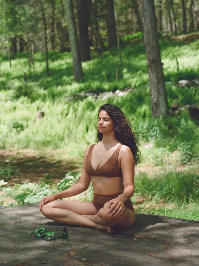 Woman meditating on a wooden deck in a forest with the ritual kit beside her