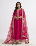 A woman models a traditional Indian outfit consisting of a bright pink kurta with gold embroidery, matching pink trousers, and a sheer pink dupatta with gold floral patterns, set against a plain white studio background.