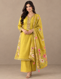 A woman models a traditional Indian salwar kameez suit in mustard yellow, featuring a kurta with floral embroidery, matching wide-leg trousers, and a coordinating dupatta draped over her shoulder.