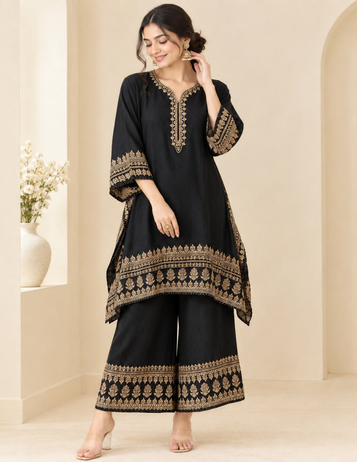 Model posing in an elegant black kaftan and palazzo set with detailed gold foil printing and embroidery against a neutral background.