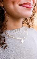 Close-up of a person wearing a gold necklace with a pendant. Taudrey Jewelry, Tidal Cuff Necklace